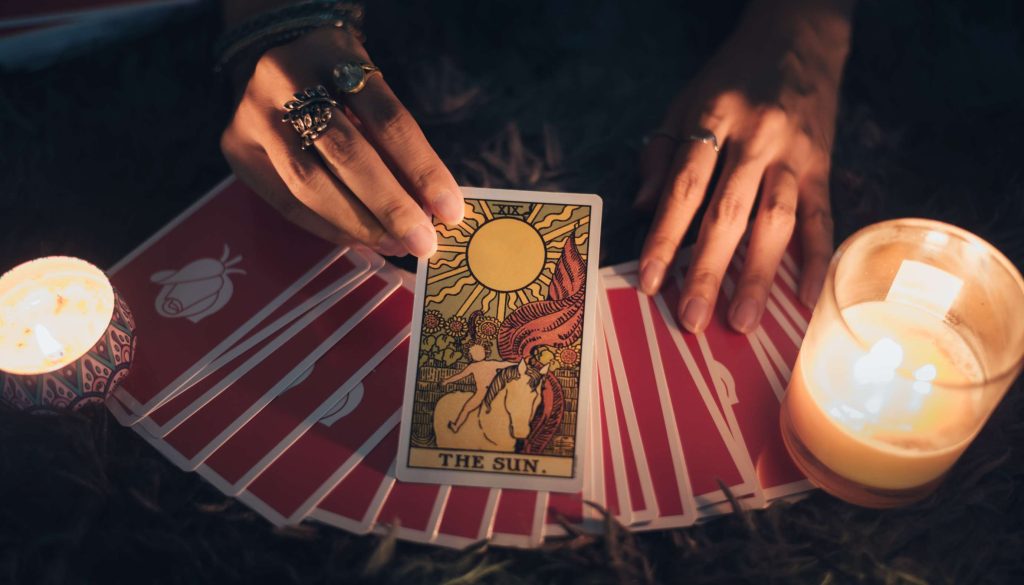 Fortune teller holding THE SUN card and tarot cards. tarot cards and burning candles. Astrologists and forecasting concept.